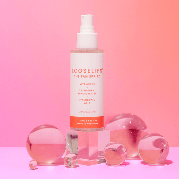 tan spritz with vitamin b5, tasmanian spring water and hyaluronic acid, gradual tan spray against peach background with crystal balls